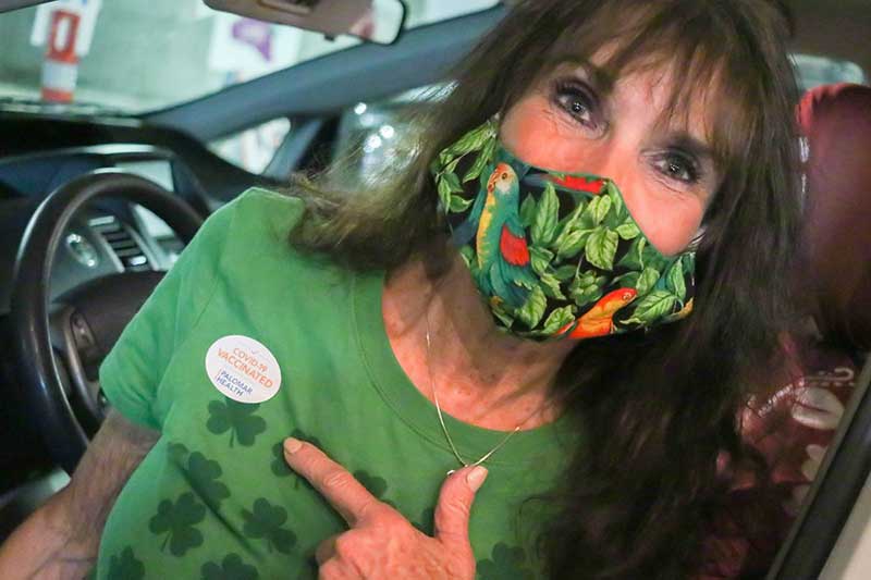 Woman wearing a green shirt with a sticker COVID-19 VACCINATED at Palomar Health